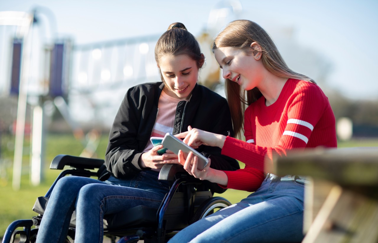 Teenage girls, one in a wheelchair, looking at each others phones