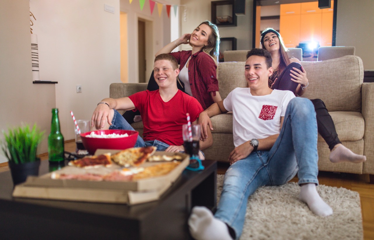 4 friends relaxing at home with food and drinks