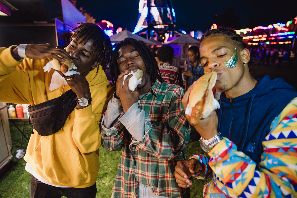 Three men eating hot dogs at a fairground