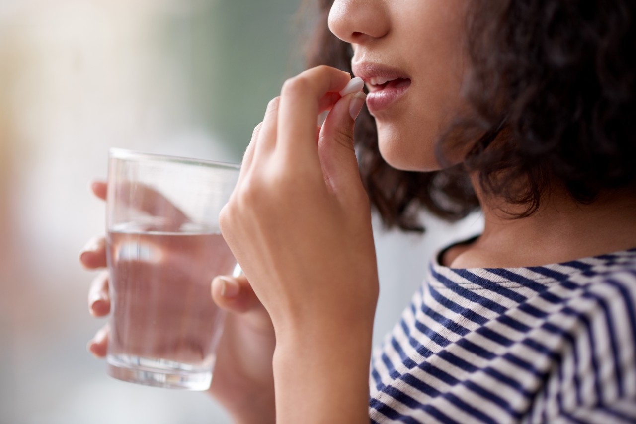 Woman with a glass of water about to take a tablet